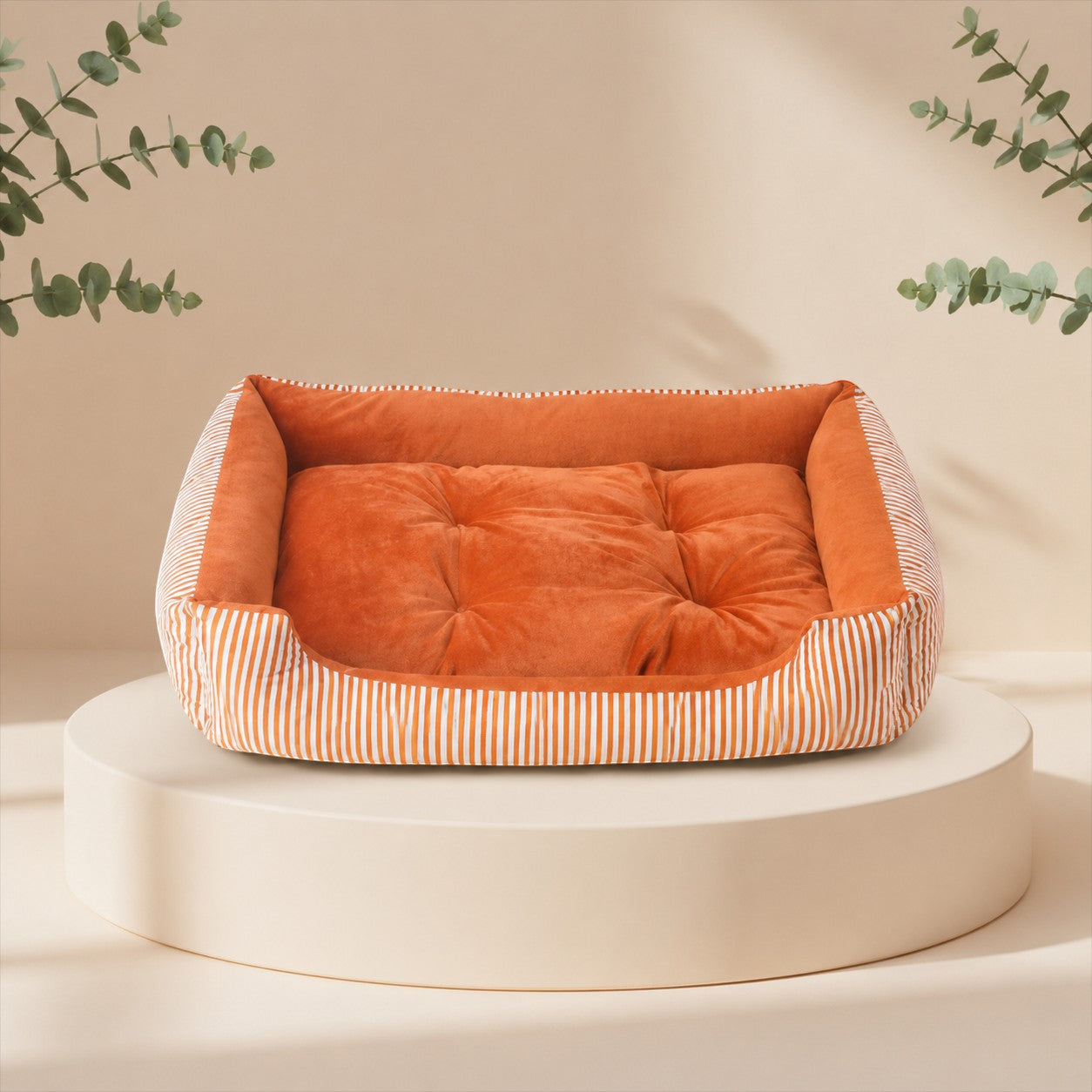 Cama nido DELONEA SnoozePup de tela suave color naranja con bordes a rayas sobre una base circular minimalista.